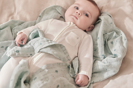 baby wearing MORI's Newborn Swaddle Bag in The Little Green Sheep Moses Basket