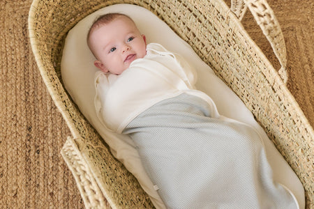 baby wearing MORI's Newborn Swaddle Bag in The Little Green Sheep Moses Basket